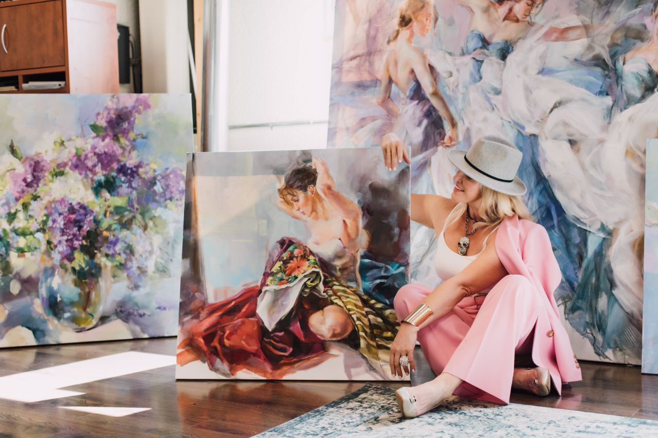 Anna Razumovskaya holding a canvas beside floral paintings